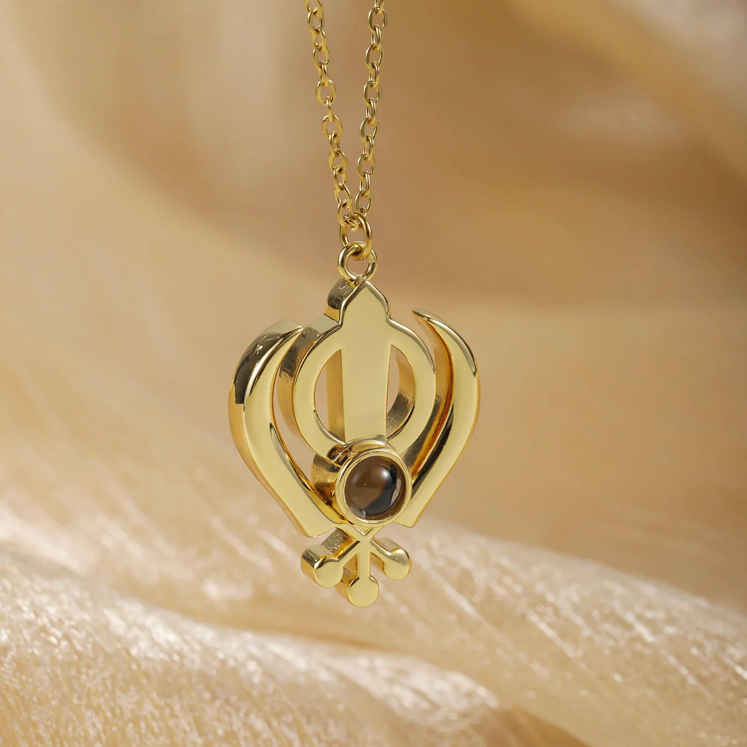 Gold 3D Khanda Pendant Necklace with a central projection stone, displayed against a soft fabric background for detail.