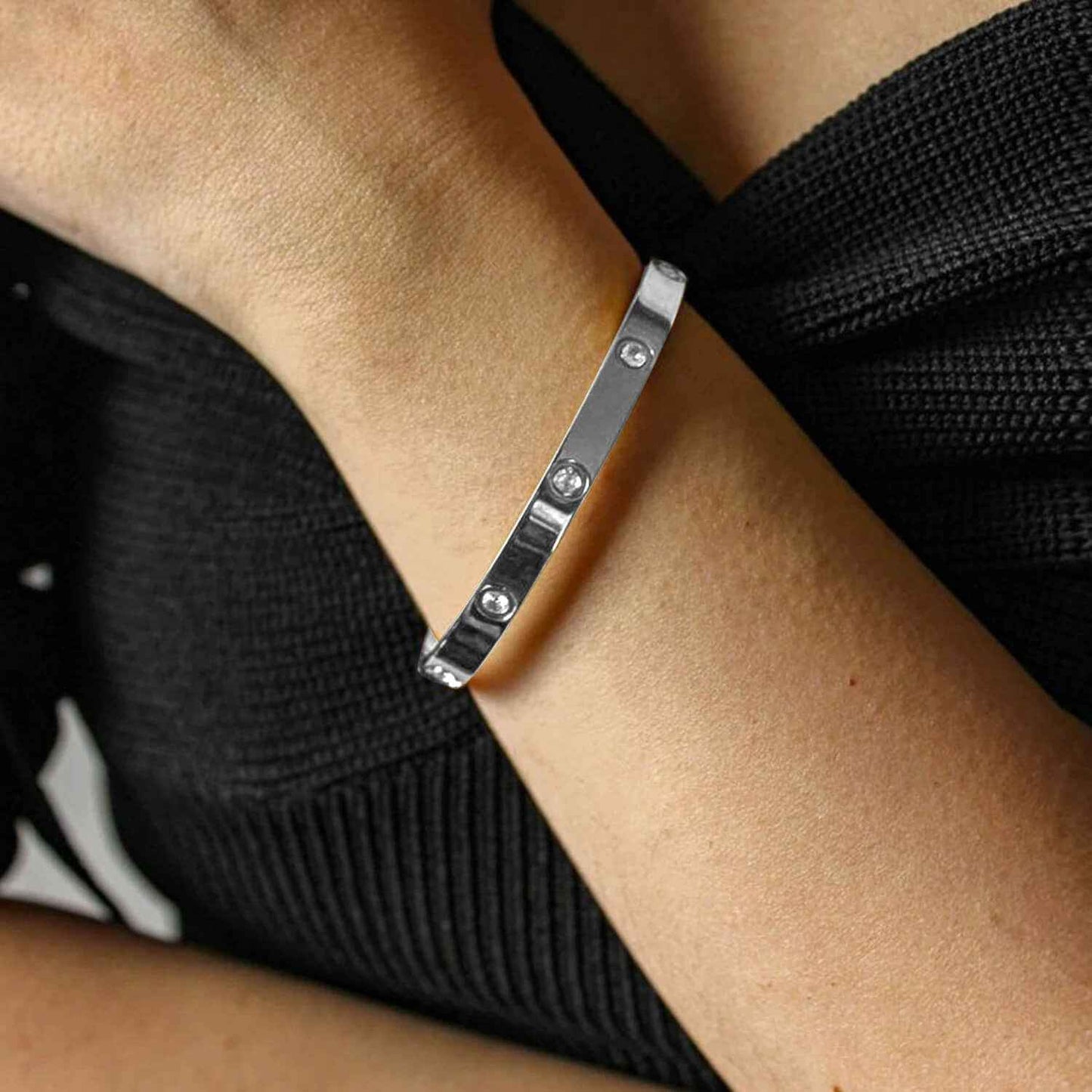 Silver minimalist love cuff bracelet on wrist, highlighting its sleek, waterproof design with embedded zirconia stones.