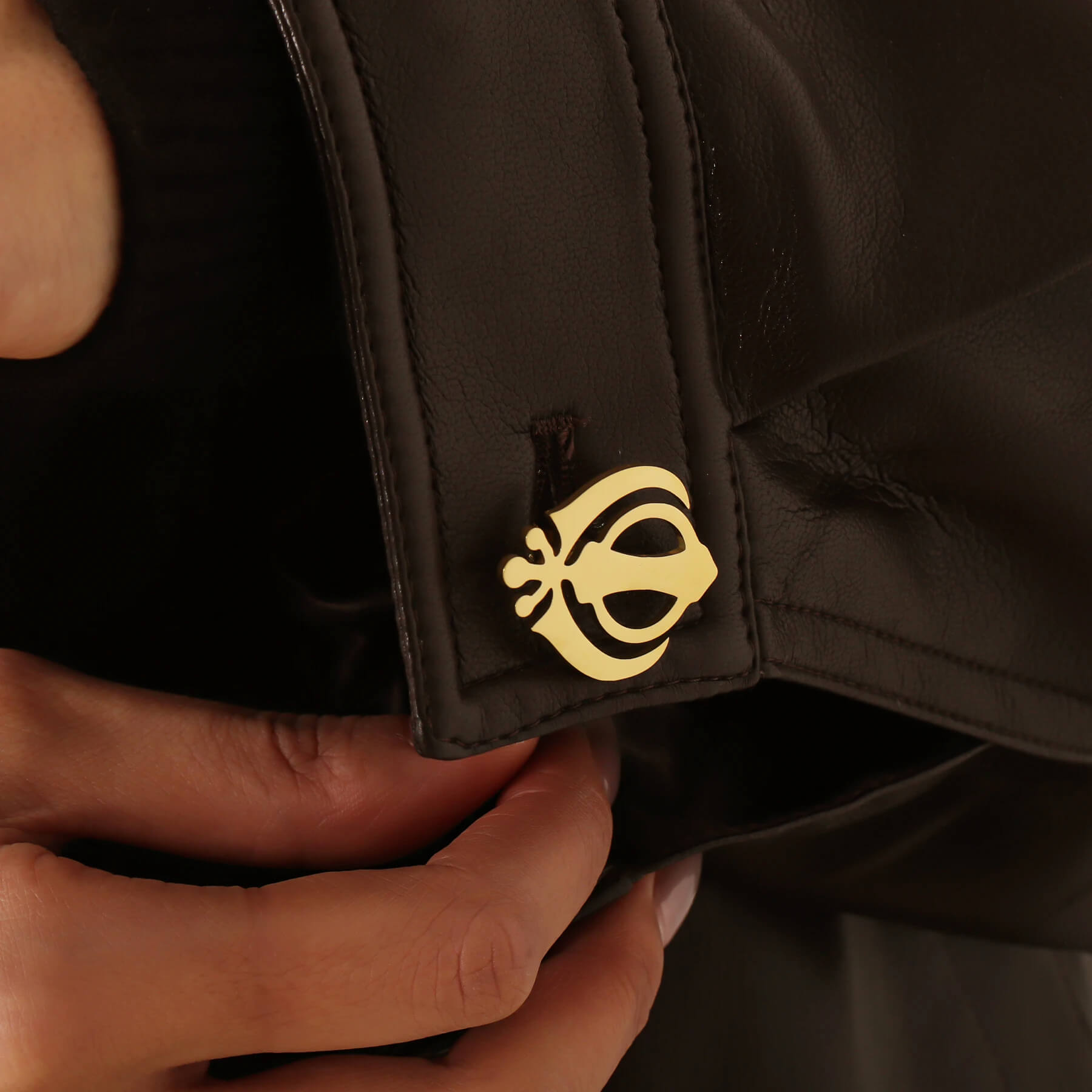 Gold Khanda cufflink styled on a black leather cuff, showcasing the Punjabi Sikh 18K stainless steel accessory in use.