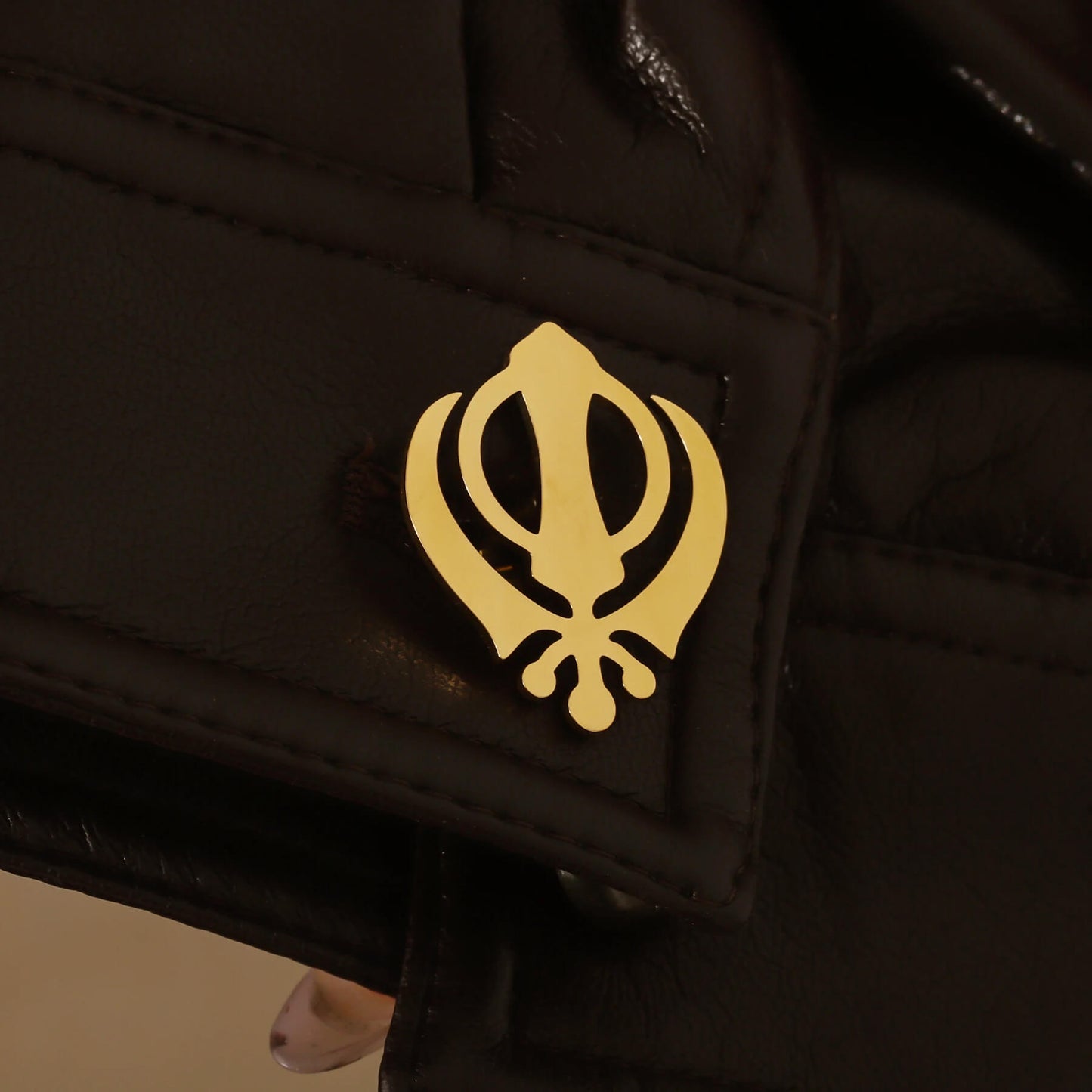 Close-up of gold Punjabi Sikh cufflink with Khanda symbol on a black leather cuff, emphasizing faith-inspired detail.