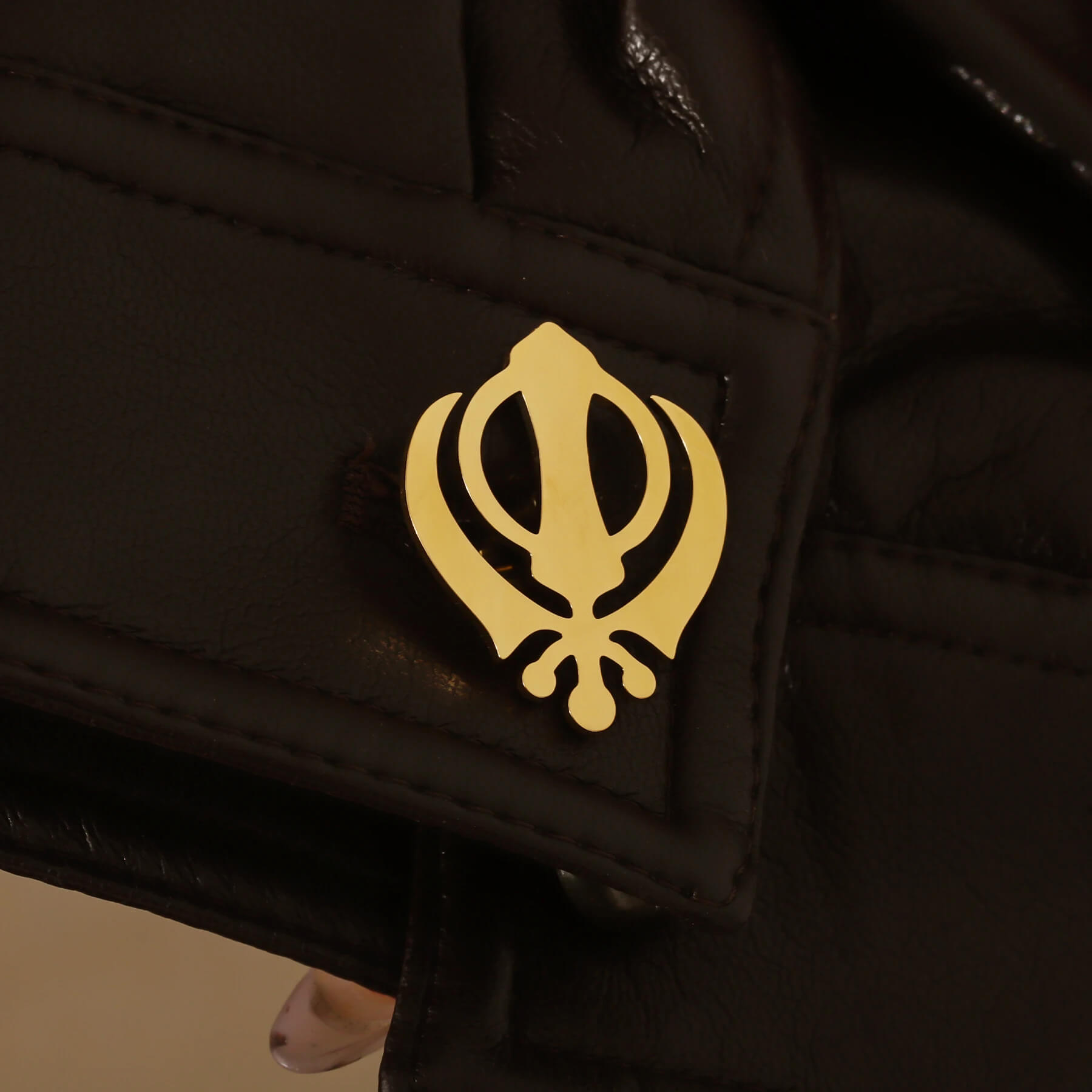 Close-up of gold Punjabi Sikh cufflink with Khanda symbol on a black leather cuff, emphasizing faith-inspired detail.