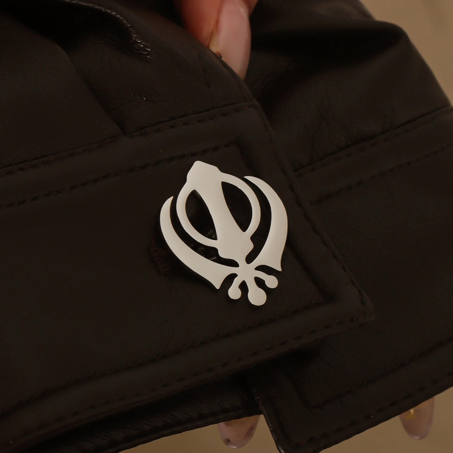 Silver Punjabi Sikh cufflink with Khanda emblem worn on a black leather cuff, showcasing stainless steel finish.