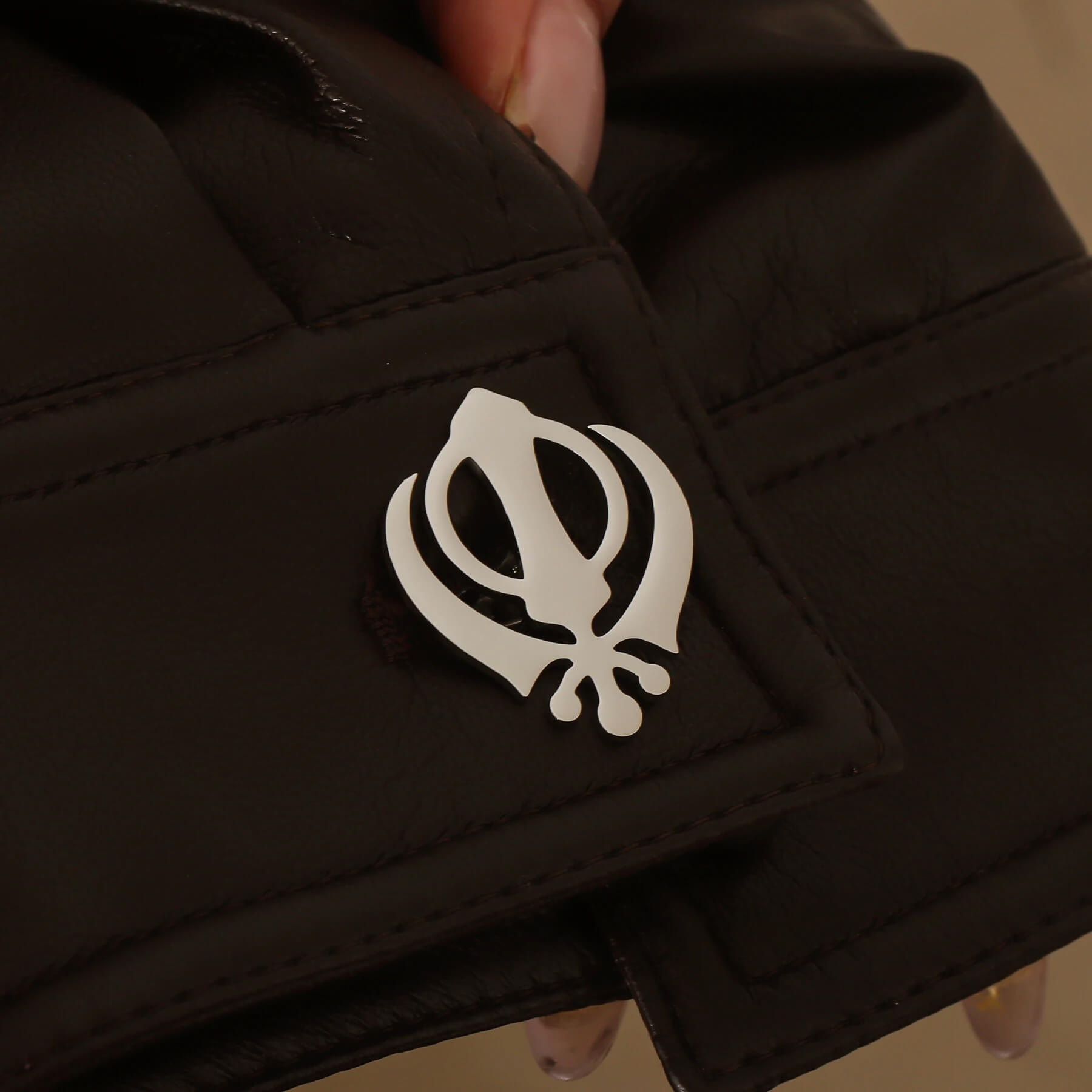 Silver Punjabi Sikh cufflink with Khanda emblem worn on a black leather cuff, showcasing stainless steel finish.