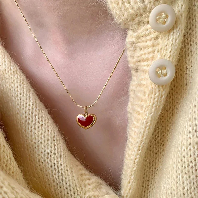 Ruby Glow Heart Necklace featuring red heart pendant on gold-tone chain against a cozy yellow sweater.