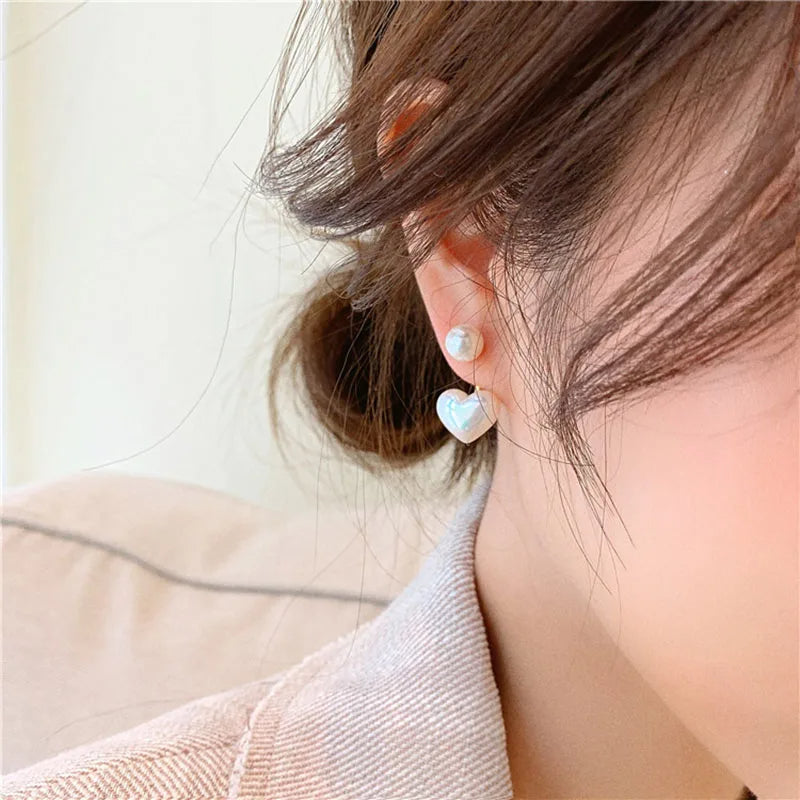 Close-up of a person wearing Dainty Love Studs Earrings with heart shape and imitation pearl details.