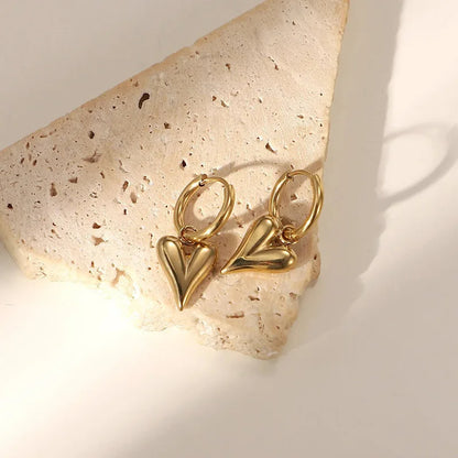 Chic heart hoop earrings with polished gold finish displayed on a textured stone background.