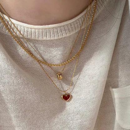 Stylish layered gold-tone necklaces featuring a ruby heart pendant on a person wearing a cozy sweater.