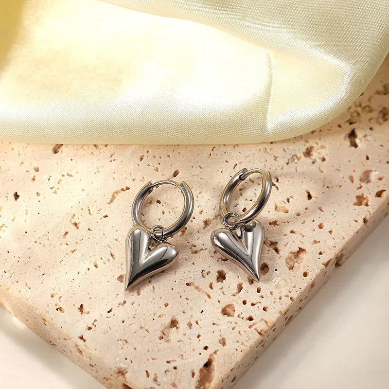 Chic Heart Hoop Earrings with polished stainless steel, featuring heart-shaped pendants, styled on a textured surface.